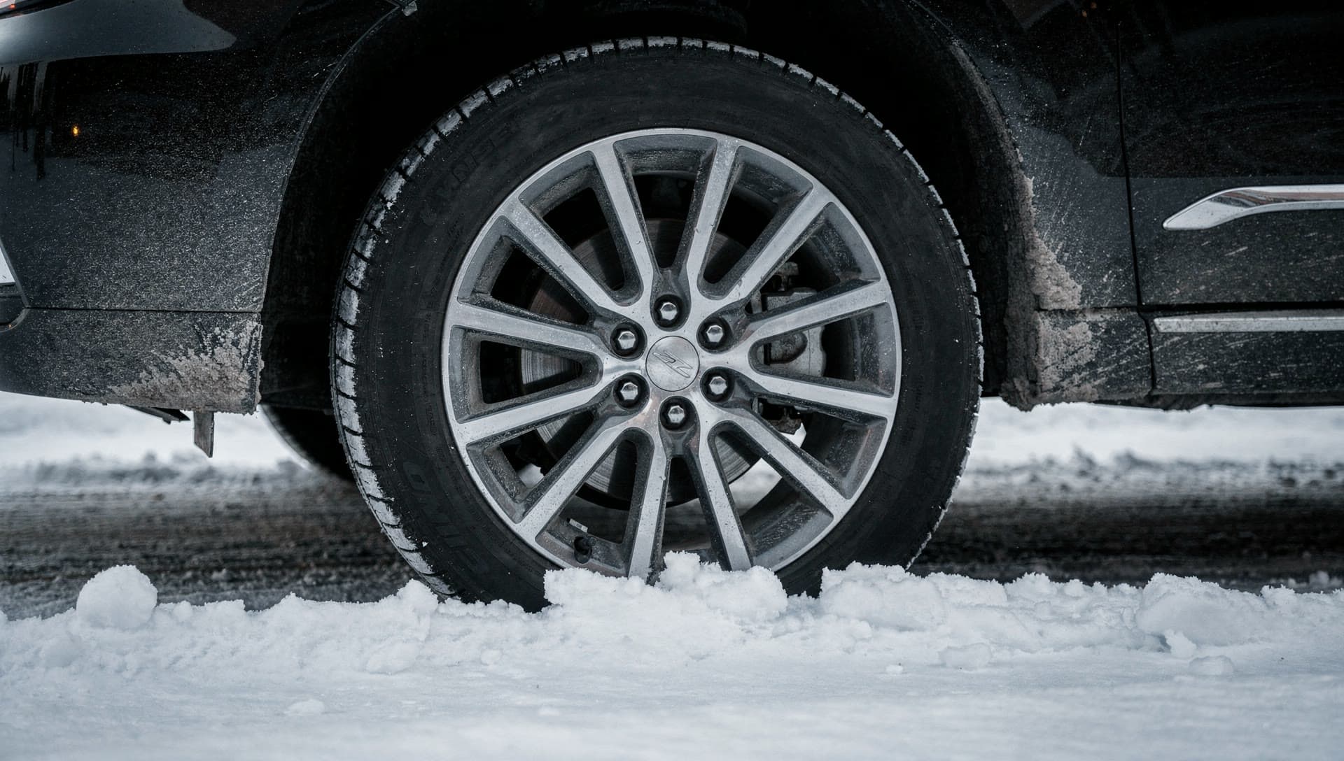 The wheel and salt-caked lower body of a black SUV standing in plowed winter slush