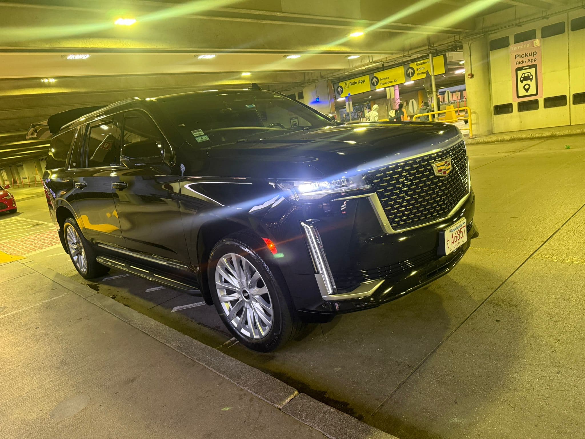 An El Khourys Cadillac Escalade waiting at Logan Airport Terminal B, terminal pickup signage visible behind the vehicle