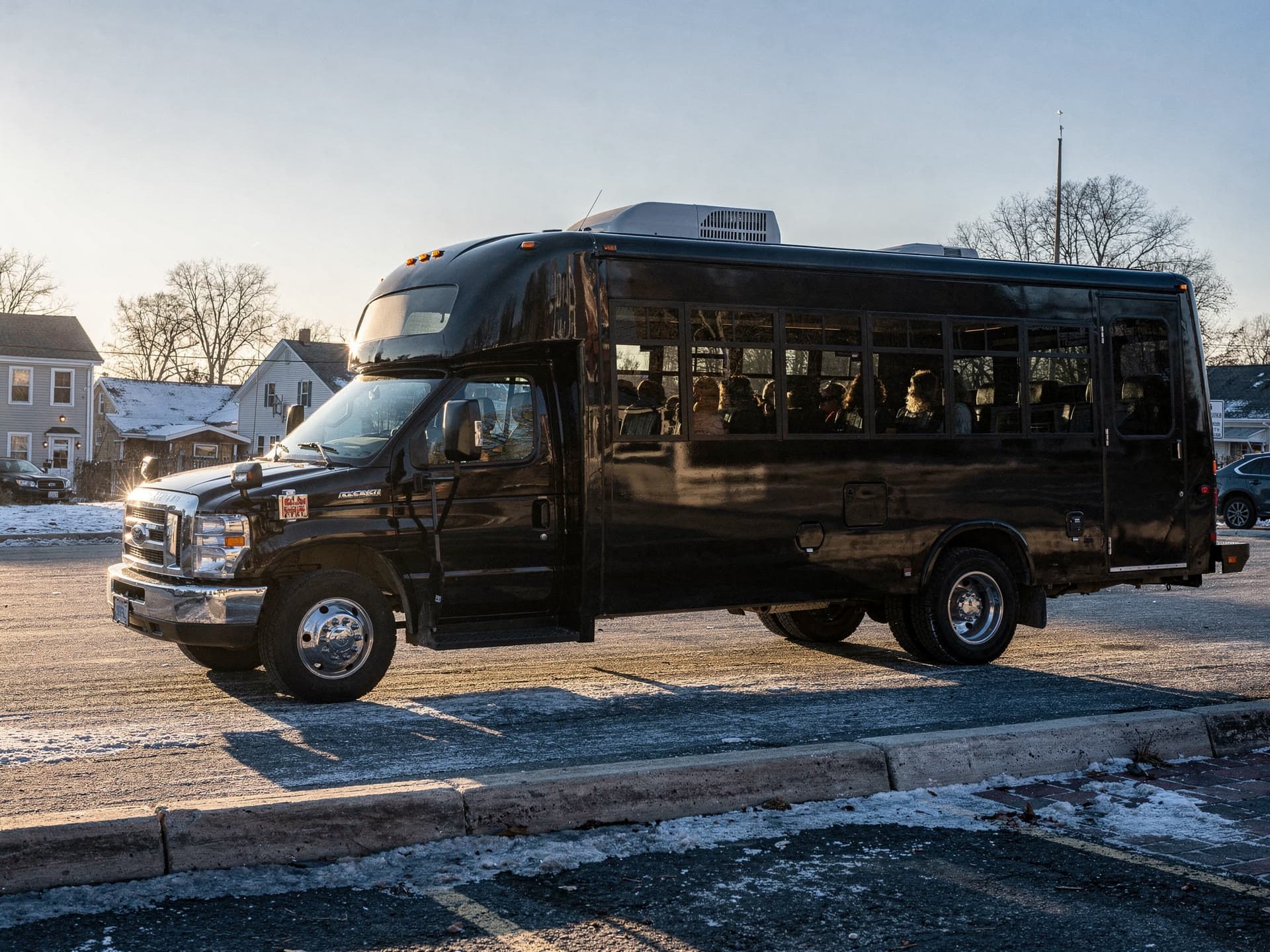A party bus pulling away from a plaza in early morning light, a handful of passengers settling into wraparound seating inside.