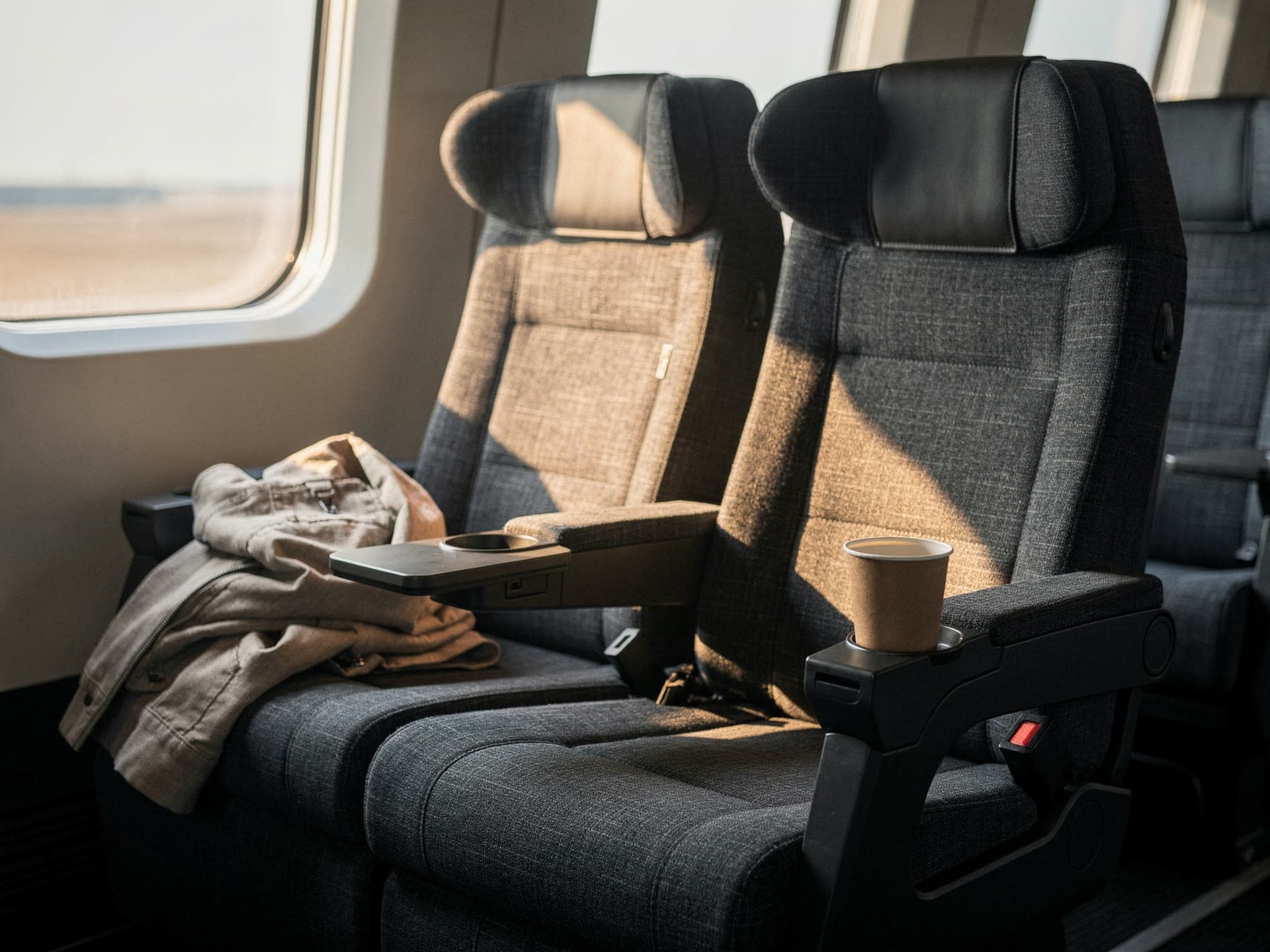 Reclining high back coach seats in morning light, a window seat with a jacket folded over the armrest.