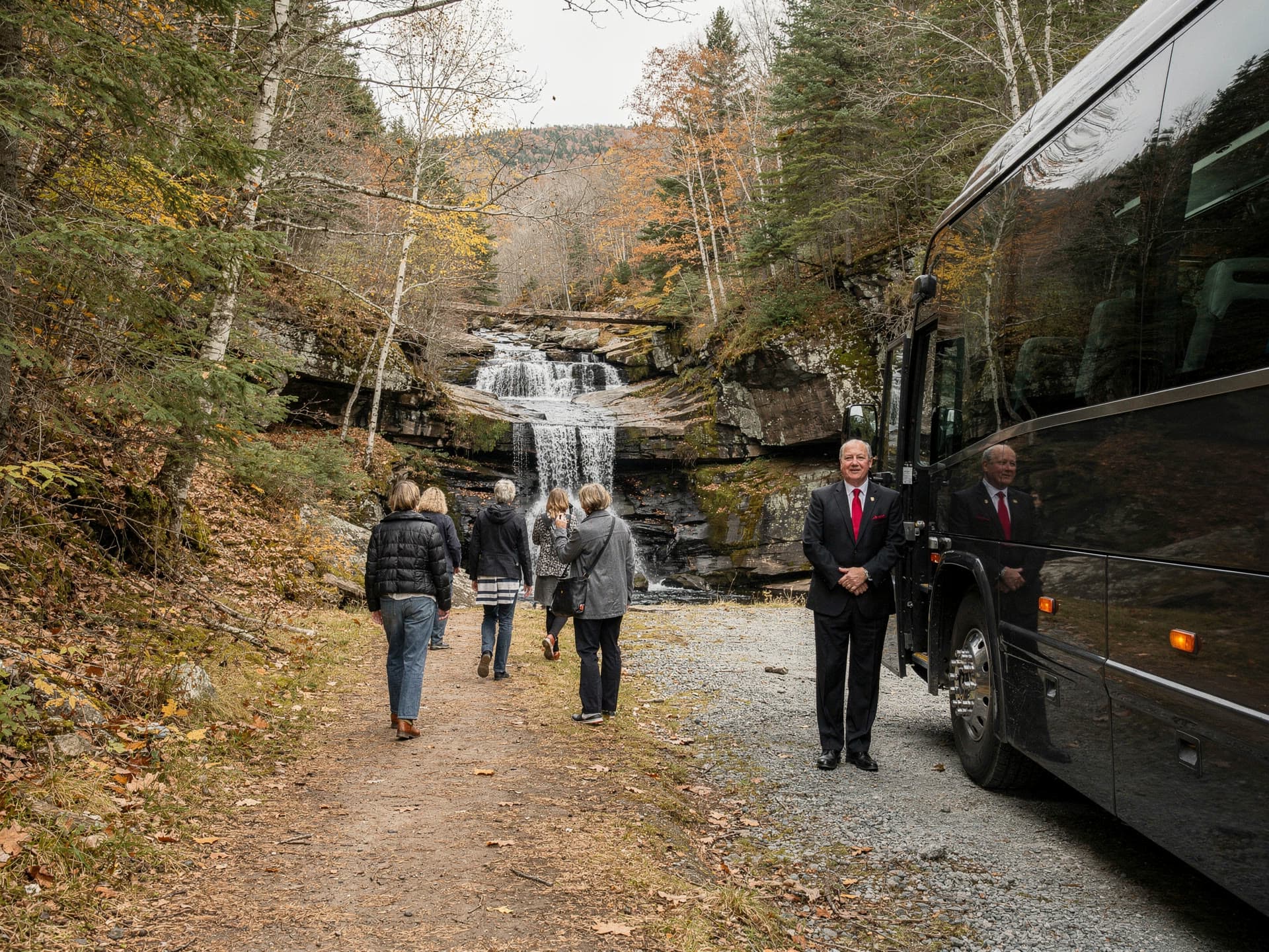 A gravel pull off beside a White Mountains waterfall, a few people walking a short trail away from a parked coach.