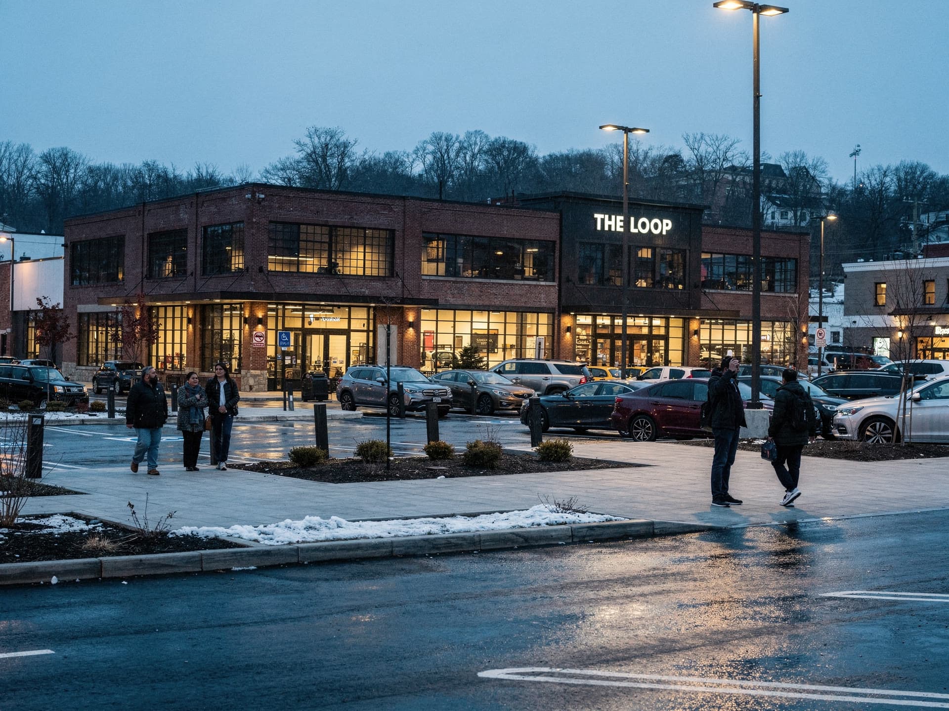 The forecourt of a Methuen plaza at dusk, small groups walking in from the parking lot toward the pickup lane.
