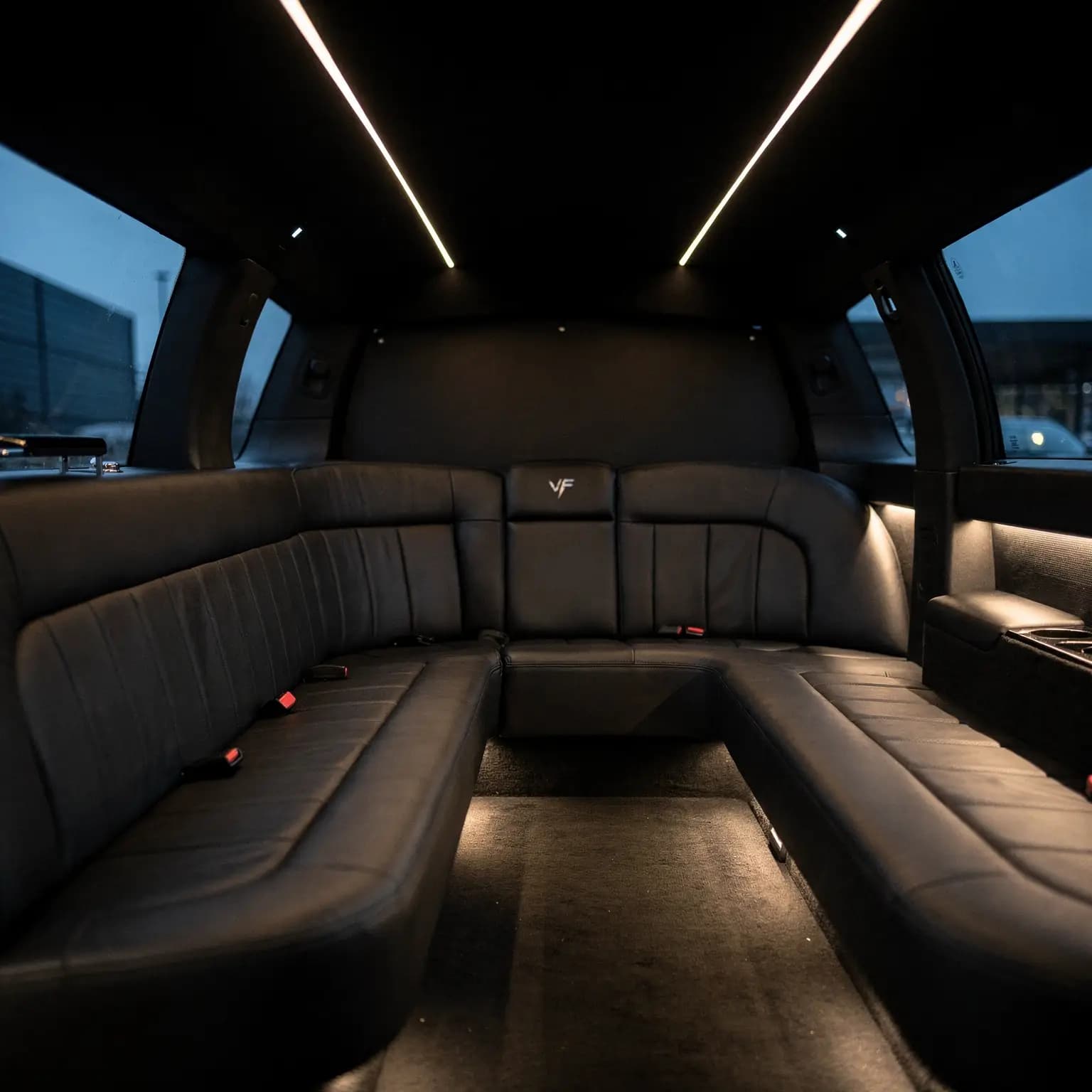 The inside of a stretch limousine before a pickup, a continuous leather bench running down both sides and across the back beneath a lit ceiling seam.
