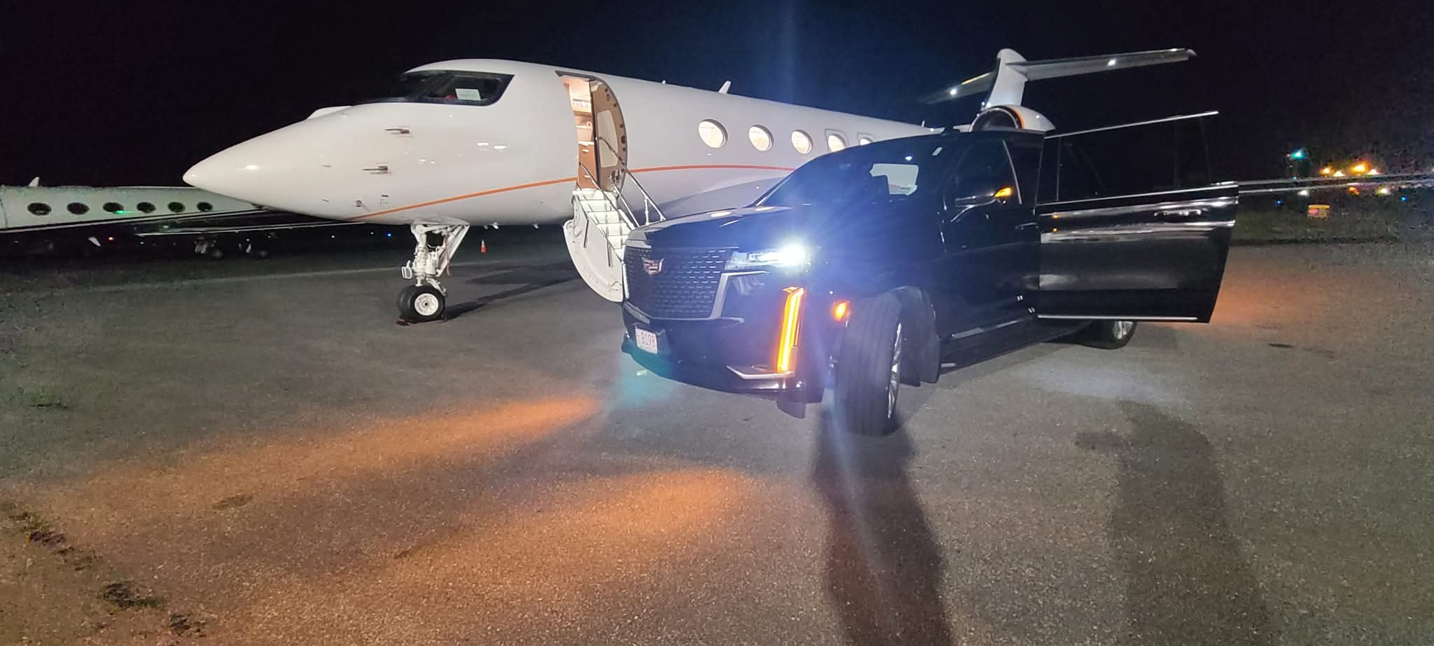 El Khourys' black Cadillac Escalade parked on a dark FBO ramp at night with its rear door open, alongside a white Gulfstream business jet with the airstair down and the cabin lit.