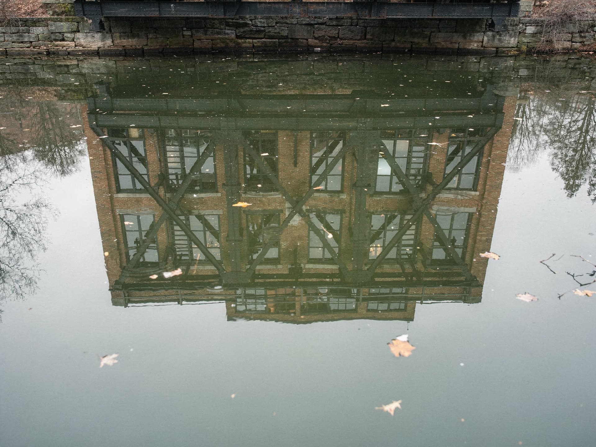 Iron canal bridge structure and mill brick reflected in still water in Lawrence.