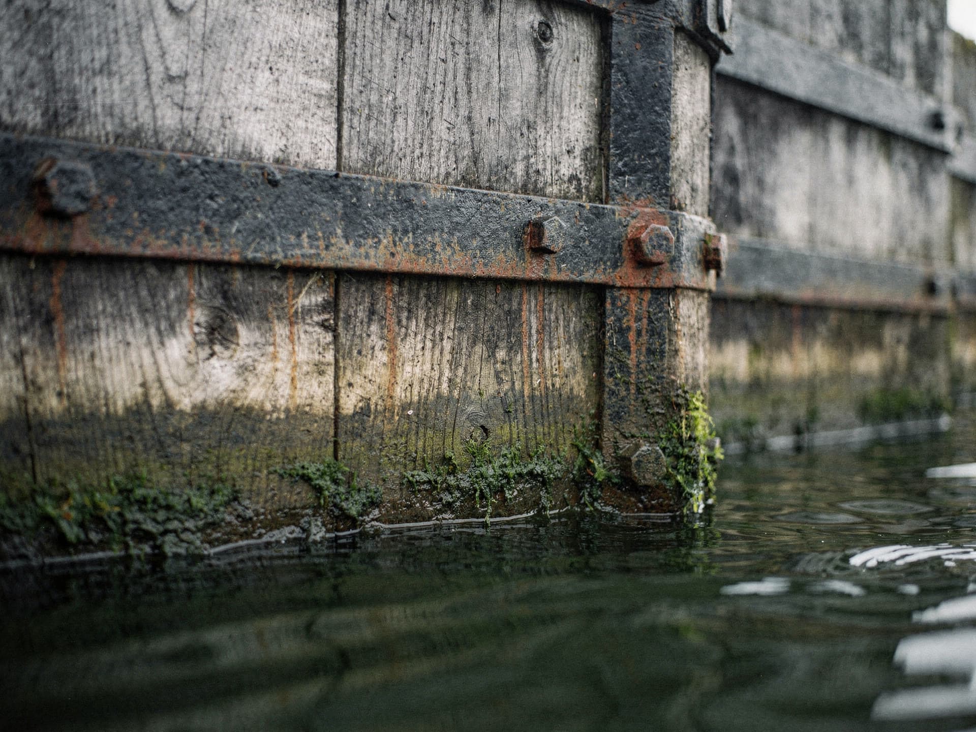 The weathered timber and iron of a canal lock gate in Lowell, water below.