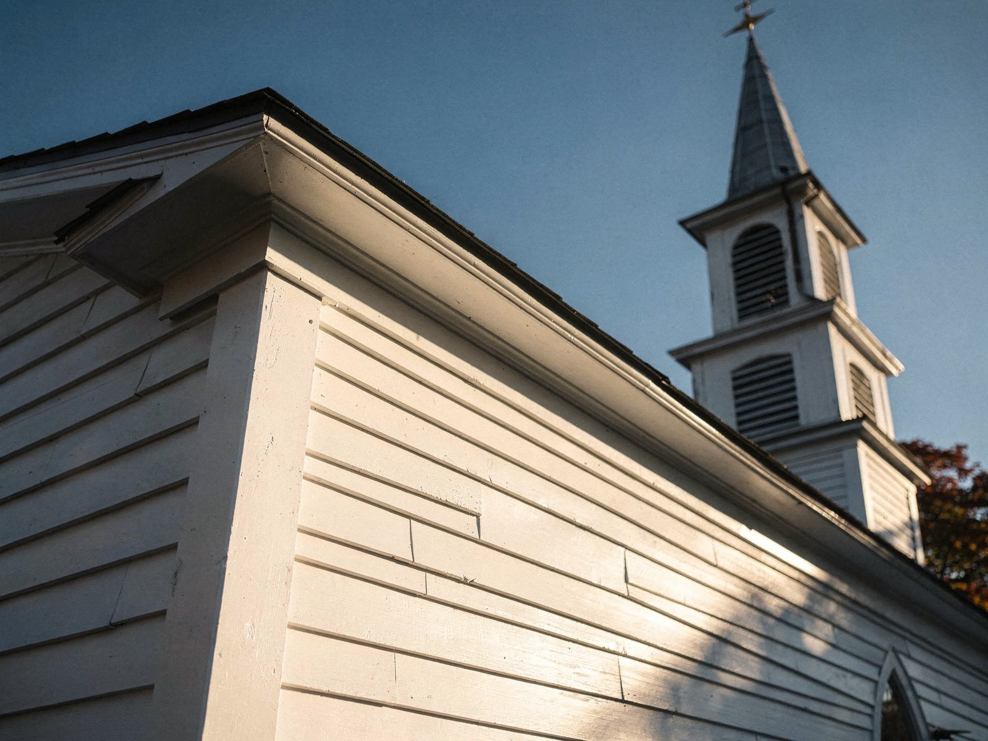 White clapboard and a steeple against a clear autumn sky, seen from a low angle.