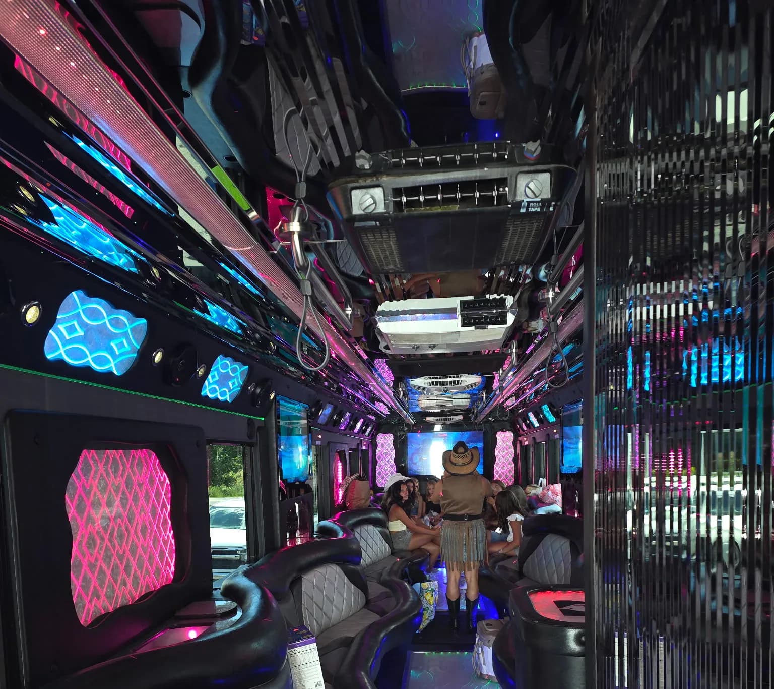 Inside a party bus lit pink and blue, a group in cowboy hats seated on the wraparound leather bench toward the back