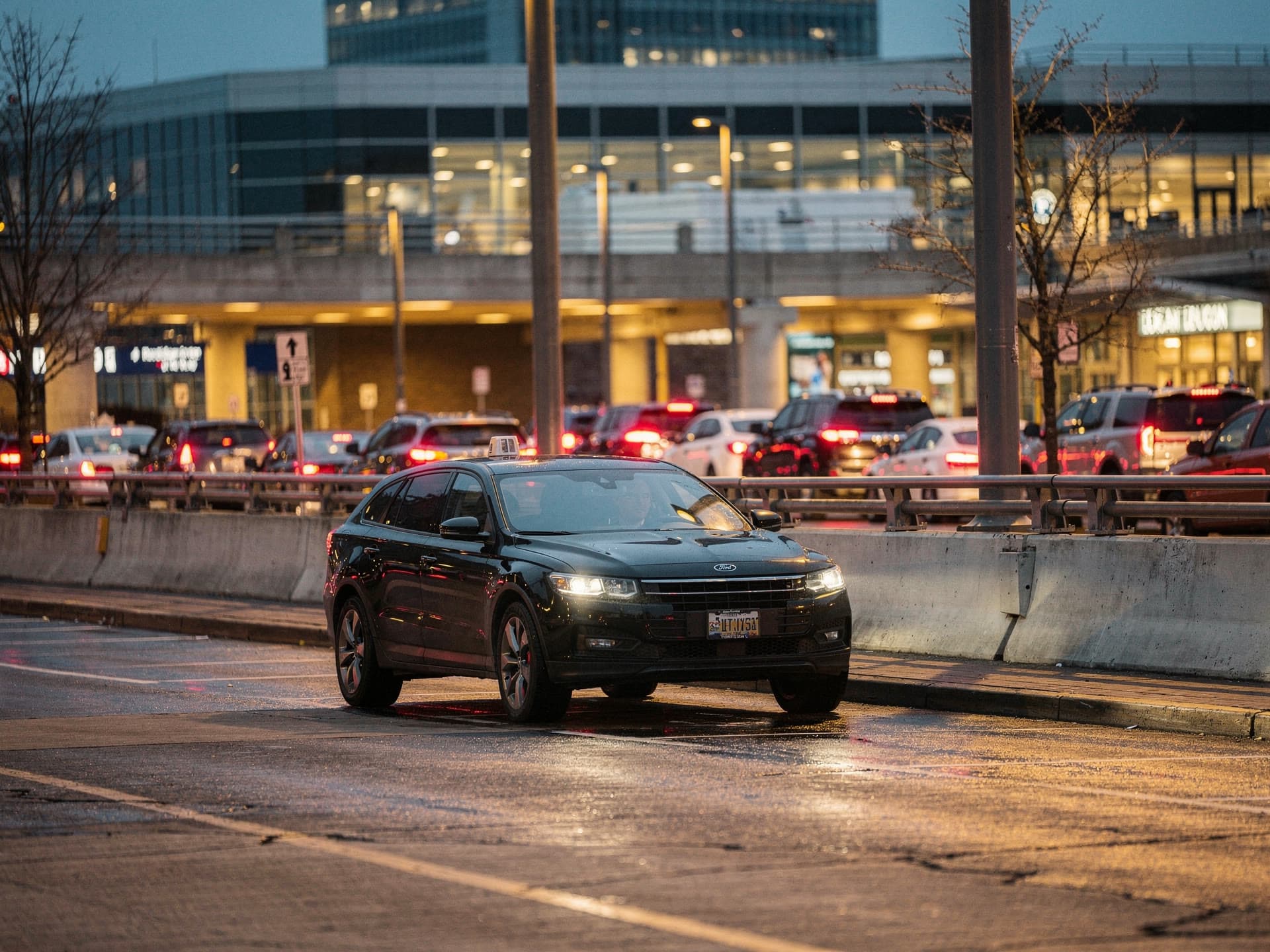 The Logan departures curb under sodium light before dawn, one black SUV at the curb and the tail lights of traffic beyond it.