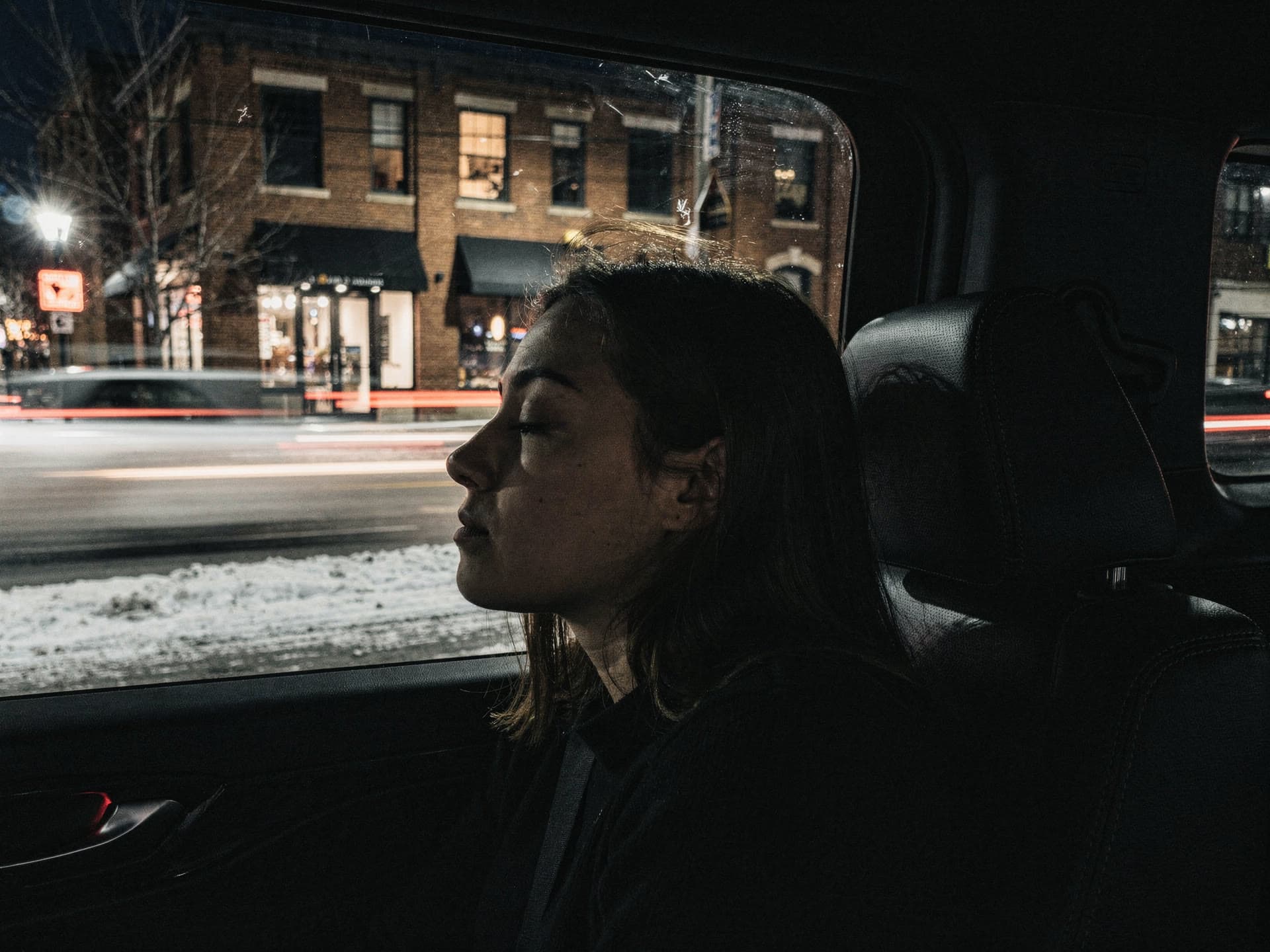 City lights streaking across a rear window in very low light, a passenger asleep against the glass on the way home.