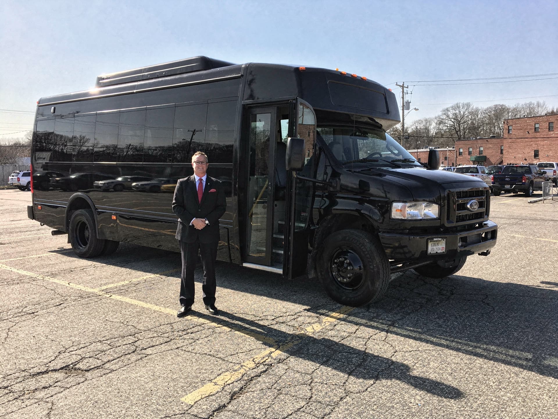The largest party bus photographed low and three quarter on in daylight, a chauffeur standing at the open door giving the vehicle scale.