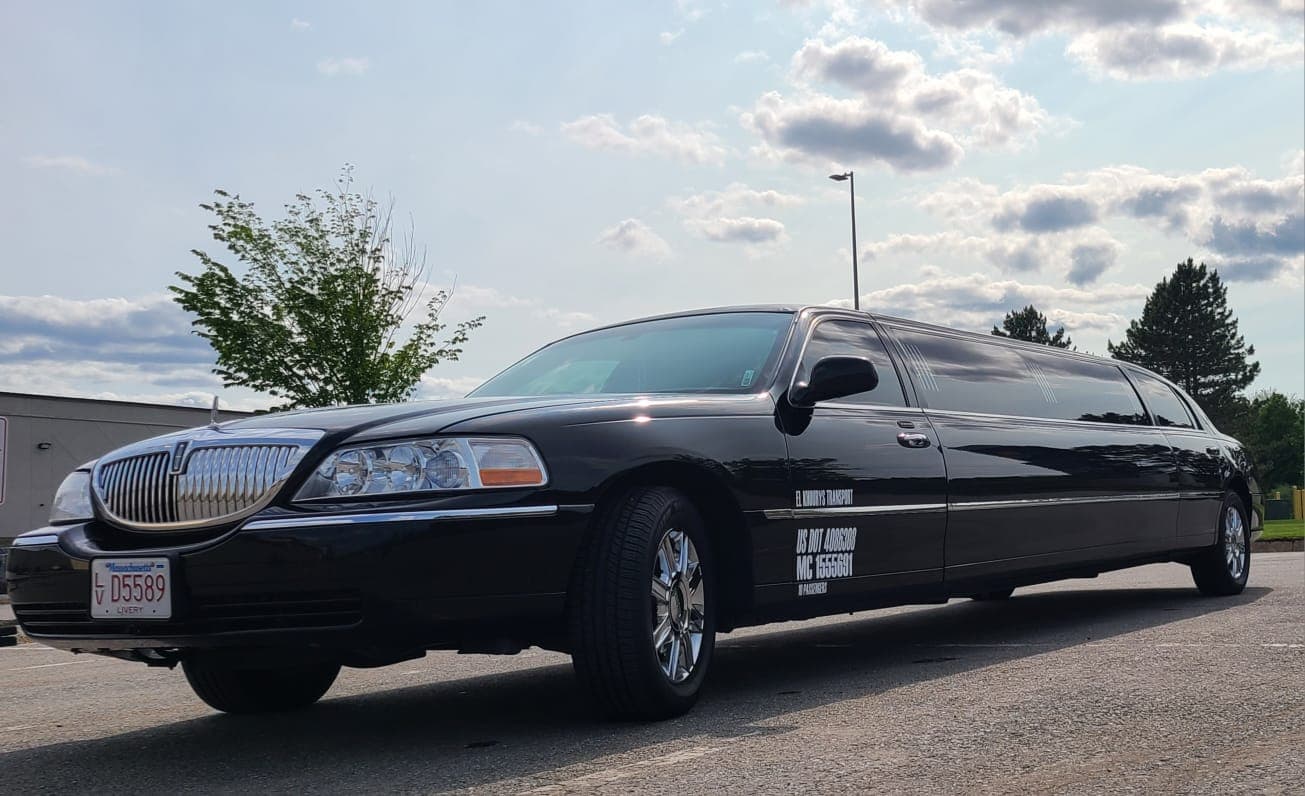 The lower door of El Khourys' black Lincoln Town Car stretch limousine in daylight, with the company name, the USDOT and MC authority numbers and the passenger count lettered along it, and a Massachusetts livery plate on the front bumper.