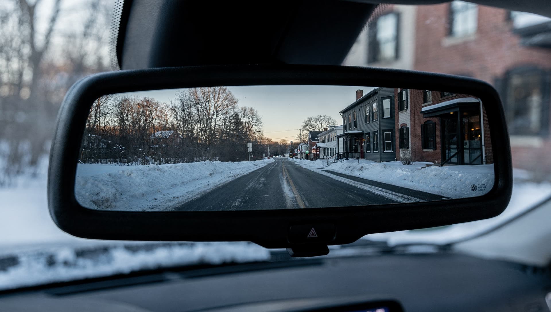 An empty road at dawn receding in a vehicle's rear-view mirror, headlights of no other traffic behind